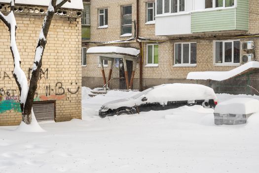Stuck cars under the snow and ice. City street after blizzard. Buried vehicle in snowdrift on the road. Parking lots in winter after heavy snowfall. Uncleaned roads. Record-breaking amounts of snow.