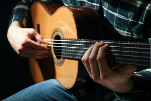 Man playing on classic guitar against dark background, closeup