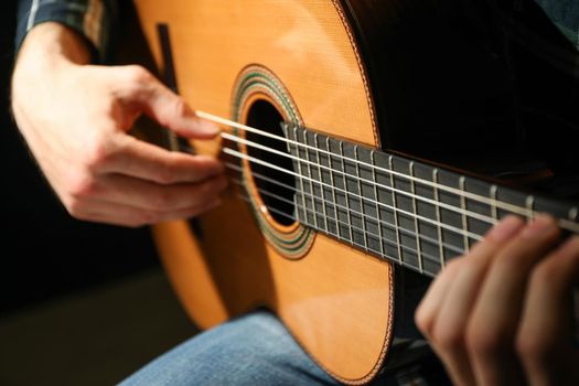 Man playing on classic guitar against dark background, closeup