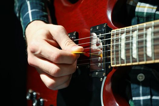 Man playing on electric guitar against dark background, closeup