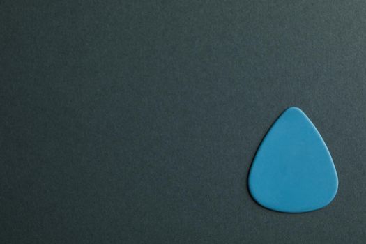 Blue guitar pick on dark background, space for text