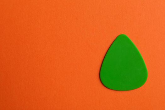 Green guitar pick on color background, space for text