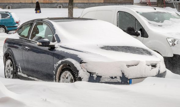 Stuck cars under the snow and ice. City street after blizzard. Buried vehicle in snowdrift on the road. Parking lots in winter after heavy snowfall. Uncleaned roads. Record-breaking amounts of snow.