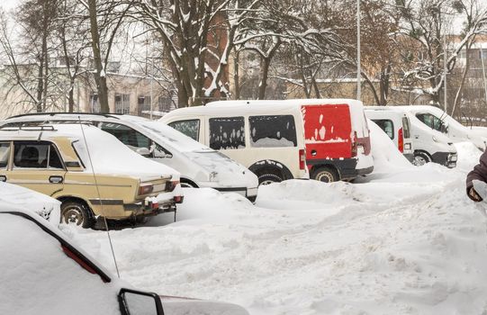 Stuck cars under the snow and ice. City street after blizzard. Buried vehicle in snowdrift on the road. Parking lots in winter after heavy snowfall. Uncleaned roads. Record-breaking amounts of snow.