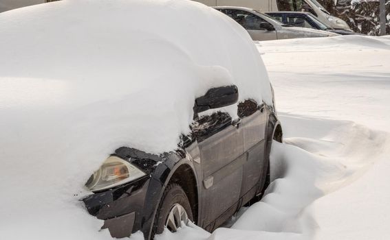 Stuck cars under the snow and ice. City street after blizzard. Buried vehicle in snowdrift on the road. Parking lots in winter after heavy snowfall. Uncleaned roads. Record-breaking amounts of snow.