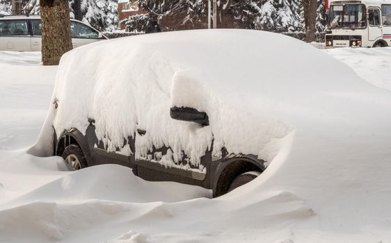 Stuck cars under the snow and ice. City street after blizzard. Buried vehicle in snowdrift on the road. Parking lots in winter after heavy snowfall. Uncleaned roads. Record-breaking amounts of snow.