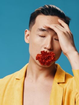 Asian man with closed eyes holds a flower in his mouth and touches his face with his hands. High quality photo