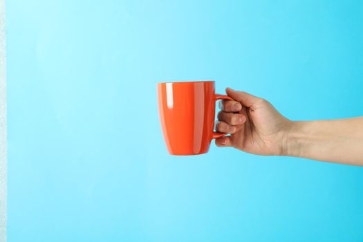 Female hand holding red cup against color background, space for text