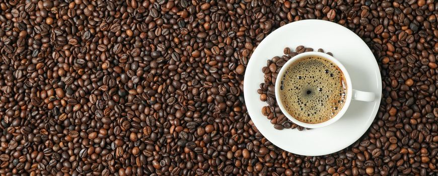 Cup of coffee with frothy foam on beans background, top view and space for text. Coffee time accessories