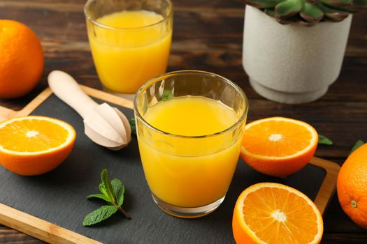 Cutting board, orange juice, wooden juicer, mint, orange, tubule and succulent plant on wooden table, closeup. Fresh natural drink and fruits