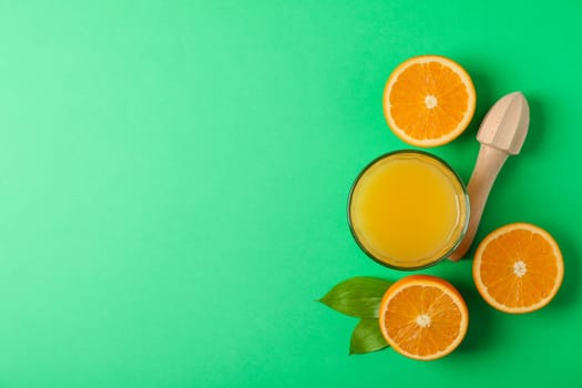Flat lay composition with fresh orange juice, wooden juicer and oranges with leaves on color background, space for text. Fresh natural drink