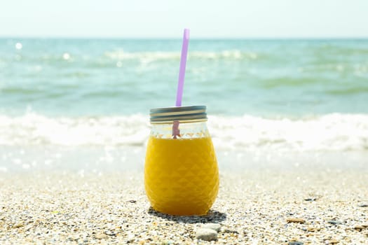 Glass jar of fresh orange juice on seaside, space for text. Summer vacation background