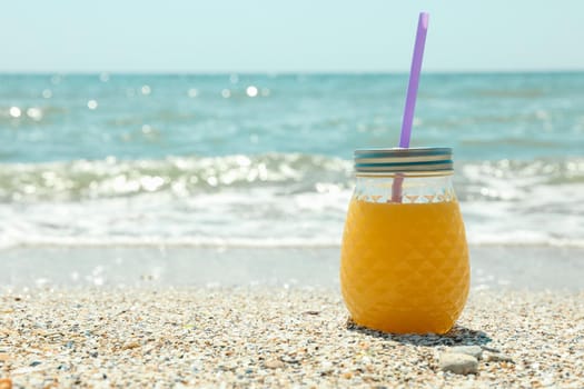 Glass jar of fresh orange juice on seaside, space for text. Summer vacation background