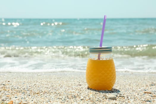 Glass jar of fresh orange juice on seaside, space for text. Summer vacation background