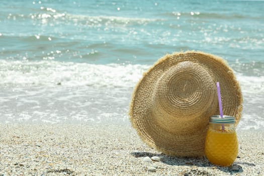 Straw hat and orange juice on seaside, space for text. Summer vacation background