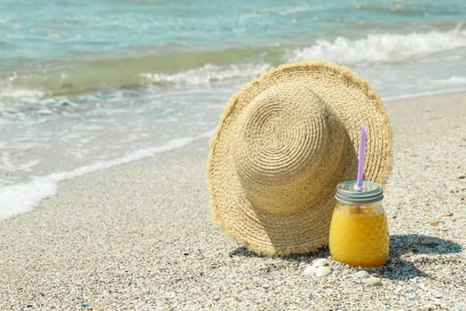 Straw hat and orange juice on seaside, space for text. Summer vacation background