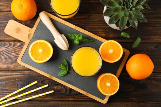 Cutting board, orange juice, wooden juicer, mint, orange, tubule and succulent plant on wooden table, top view. Fresh natural drink and fruits