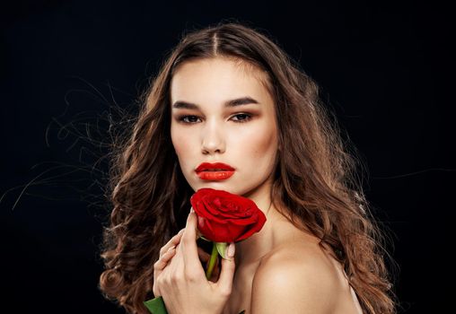 Brunette woman with a red rose in her hand on a dark background close-up. High quality photo