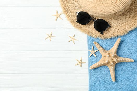 Straw hat, sunglasses, towel and starfishes on white wooden background, space for text and top view. Summer vacation backdrop
