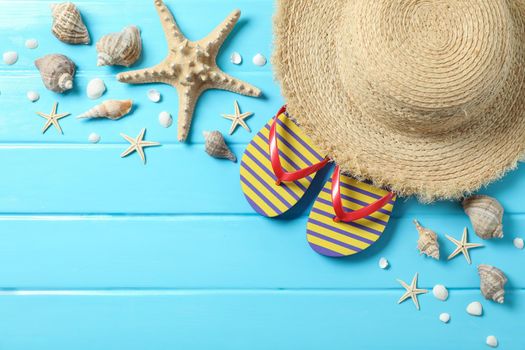 Straw hat, flip flops and many starfishes on color wooden background, space for text and top view. Summer vacation backdrop