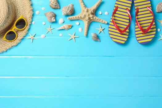 Straw hat, sunglasses, flip flops and many starfishes on color wooden background, space for text and top view. Summer vacation backdrop