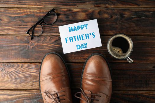 Brown leather shoes, inscription happy fathers day, cup of coffee and glasses on wooden background, space for text and top view