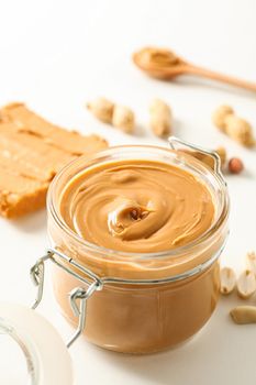 Composition with peanut butter sandwich, glass jar, peanut and spoon on white background, space for text and closeup