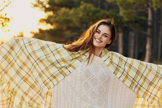 Happy woman in a sweater with a checkered plaid on her shoulders have fun near the forest and coniferous trees. High quality photo