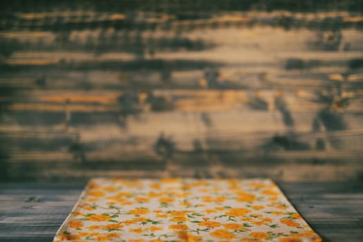 A fabric towel with a yellow floral pattern, lies on a wooden floor with a wooden background