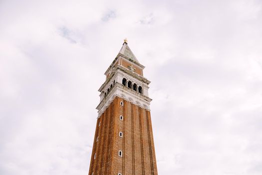 A huge bell tower made of red brick in Piazza San Marco in Venice, Italy. Against background of a cloudy, evening, October sunset sky.