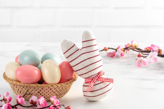 Close up of colorful Easter eggs in the nest with pink plum flower on bright white wooden table background.