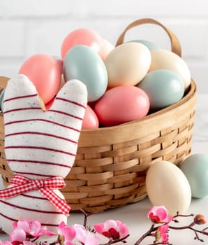 Close up of colorful Easter eggs in the nest with pink plum flower on bright white wooden table background.
