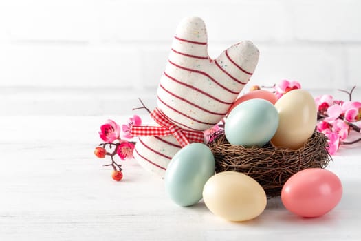 Close up of colorful Easter eggs in the nest with pink plum flower on bright white wooden table background.