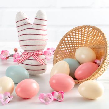 Close up of colorful Easter eggs in the nest with pink plum flower on bright white wooden table background.