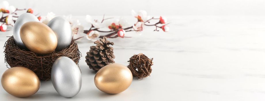 Close up of golden and silver Easter eggs in the nest with white plum flower on bright white wooden table background.