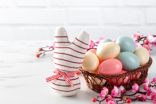 Close up of colorful Easter eggs in the nest with pink plum flower on bright white wooden table background.
