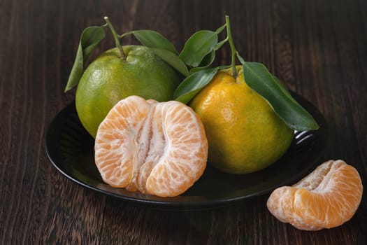 Fresh green tangerine mandarin orange with fresh leaves on dark wooden table background harvest concept.