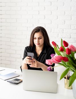 Small business concept. Young serious brunette business woman florist communicating on the phone, working at the office, bucket of tulips on the desk