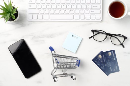 Top view of online shopping concept with credit card, smart phone and computer isolated on office marble white table background.