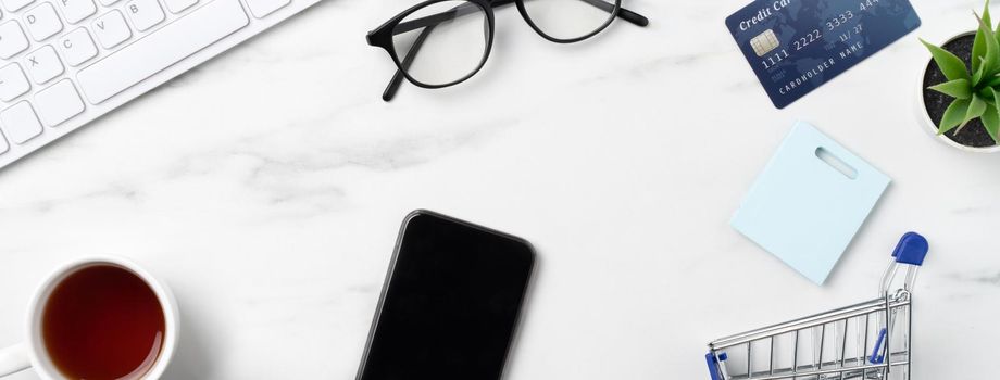 Top view of online shopping concept with credit card, smart phone and computer isolated on office marble white table background.