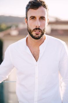 Stylish bearded guy in white shirt and light trousers on a rooftop terrace in Florence, Italy