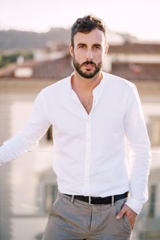 Stylish bearded guy in white shirt and light trousers on a rooftop terrace in Florence, Italy