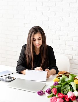 Small business concept. Spring holidays. Business woman making notes in blank desk calendar, working with flowers at the office. Mock up design