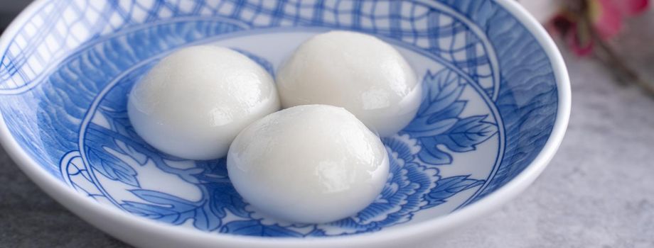 Close up of yuanxiao tangyuan (glutinous rice dumpling balls) in a bowl on gray table with flower, food for Chinese Lantern Yuanxiao Festival.