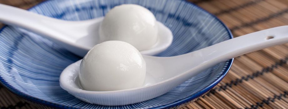 Close up of yuanxiao tangyuan (glutinous rice dumpling balls) in a bowl on gray table with flower, food for Chinese Lantern Yuanxiao Festival.