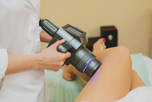 Cosmetologist doing massage with apparatus on female client legs, close up.