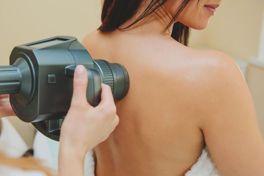 Cosmetologist doing massage with apparatus on female back, close up.