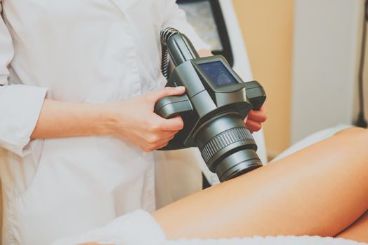 Cosmetologist doing massage with apparatus on female client legs, close up.