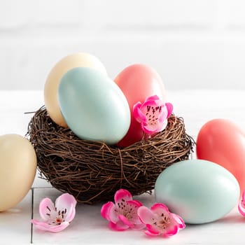 Close up of colorful Easter eggs in the nest with pink plum flower on bright white wooden table background.