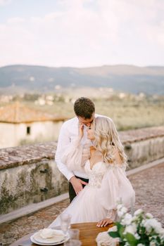 Wedding at an old winery villa in Tuscany, Italy. The groom hugs and kisses bride on the roof of an old villa.